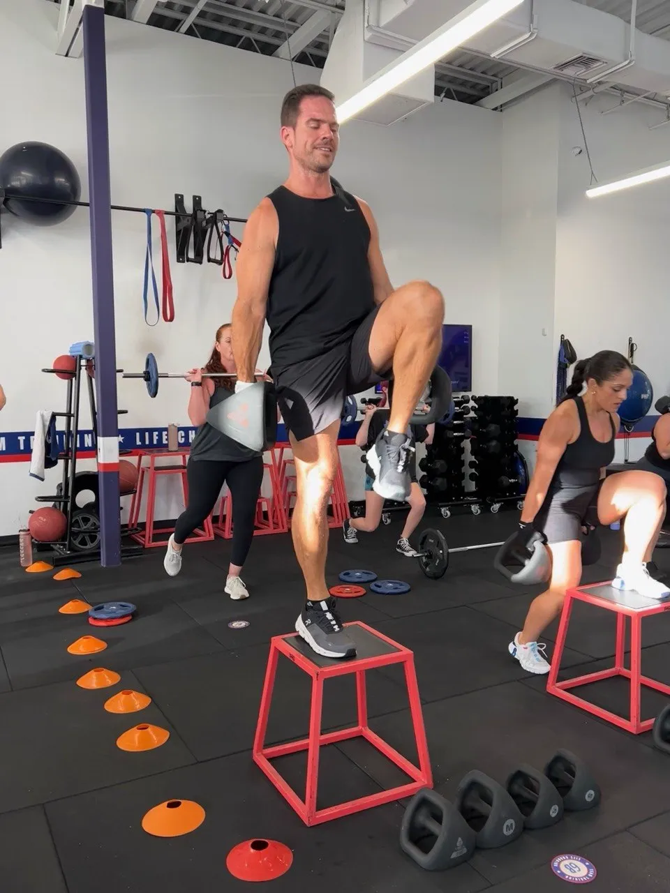 F45 Cooper City member doing step-ups on a red plyo box while others train behind